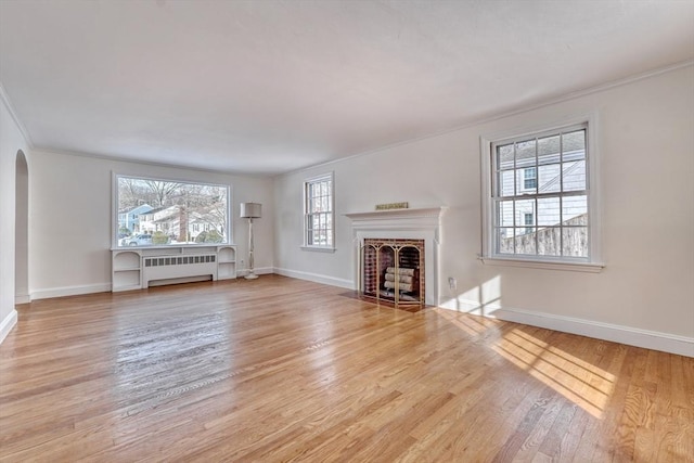 unfurnished living room with radiator, wood finished floors, a fireplace with flush hearth, arched walkways, and ornamental molding