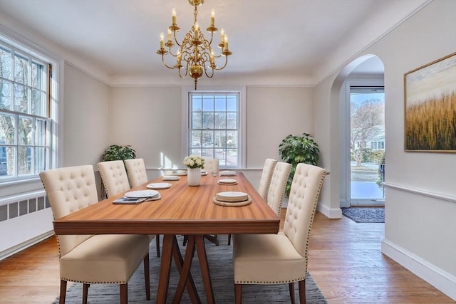 dining area with wood finished floors, baseboards, an inviting chandelier, arched walkways, and ornamental molding