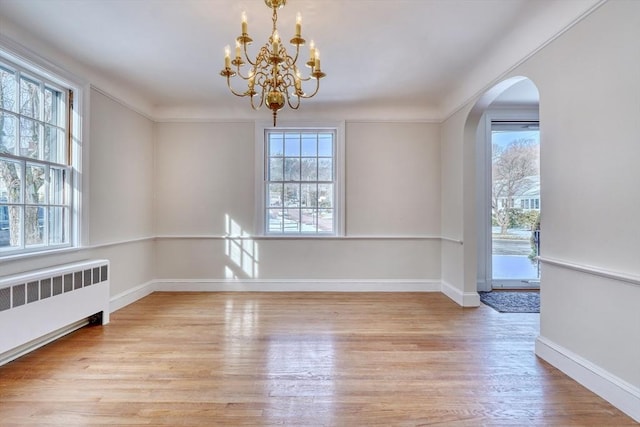 unfurnished dining area featuring arched walkways, radiator, a healthy amount of sunlight, and wood finished floors