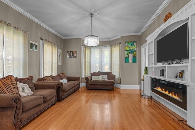 living room with light wood finished floors, crown molding, baseboards, an inviting chandelier, and a glass covered fireplace