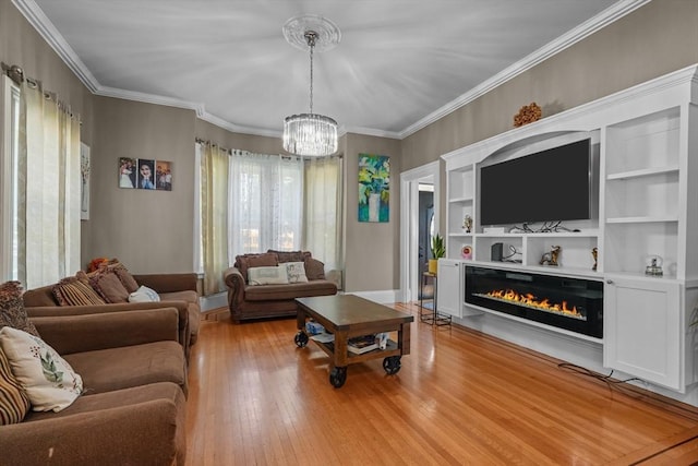 living area with baseboards, a glass covered fireplace, ornamental molding, light wood-style floors, and a notable chandelier