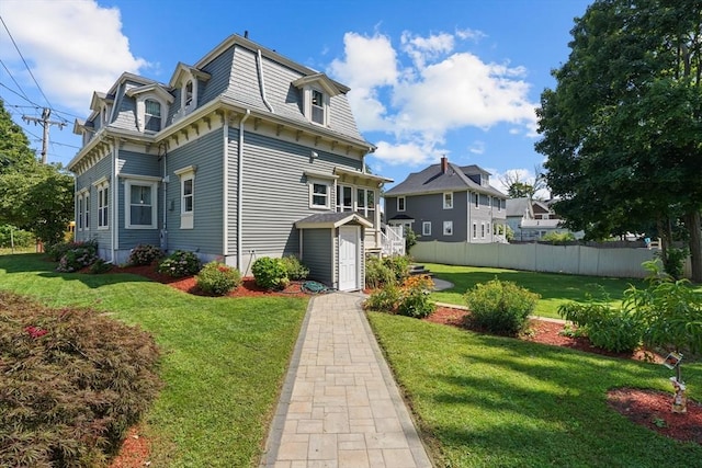 back of property with mansard roof, a yard, and fence