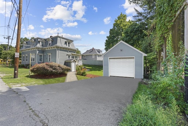 view of front of house featuring mansard roof, a detached garage, an outdoor structure, and a front yard