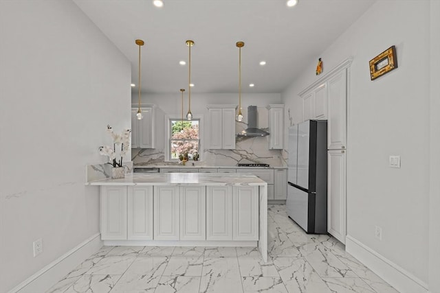 kitchen featuring baseboards, a peninsula, recessed lighting, freestanding refrigerator, and wall chimney range hood