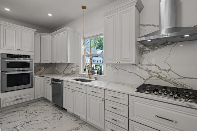 kitchen with wall chimney range hood, light stone countertops, white cabinets, stainless steel appliances, and a sink