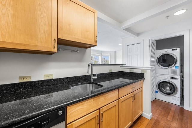 kitchen with stacked washer / drying machine, a sink, dishwashing machine, dark wood-type flooring, and dark stone countertops