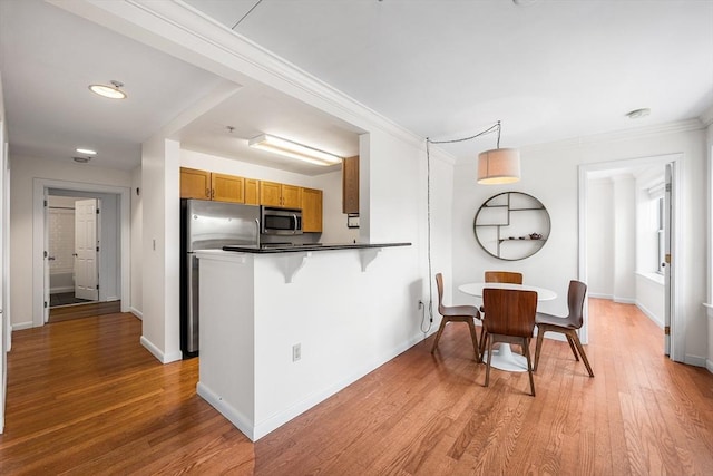 kitchen featuring appliances with stainless steel finishes, brown cabinets, dark countertops, light wood-type flooring, and a peninsula