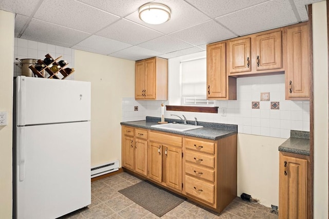 kitchen with decorative backsplash, a sink, dark countertops, freestanding refrigerator, and a baseboard radiator