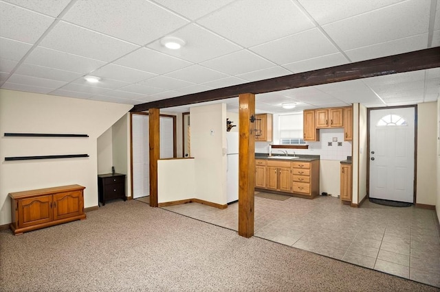 unfurnished living room with a sink, baseboards, light carpet, and a drop ceiling