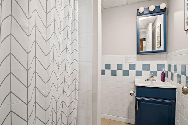 full bath featuring tile patterned flooring, a shower, tile walls, and vanity