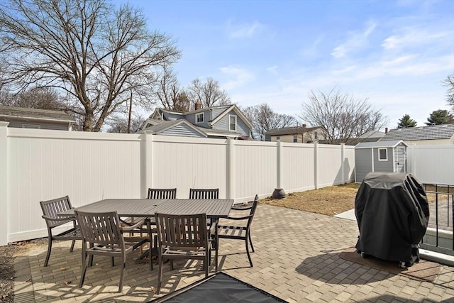 view of patio featuring outdoor dining space, a fenced backyard, an outdoor structure, grilling area, and a storage shed