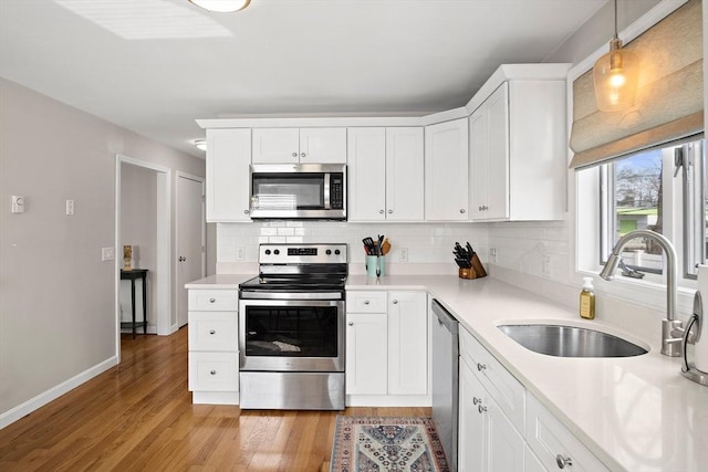 kitchen featuring light wood finished floors, a sink, stainless steel appliances, white cabinetry, and tasteful backsplash