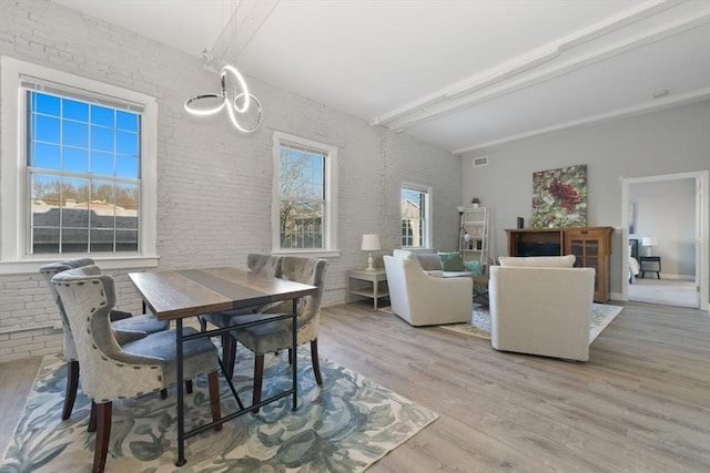 dining space with light wood-type flooring, beam ceiling, visible vents, and brick wall