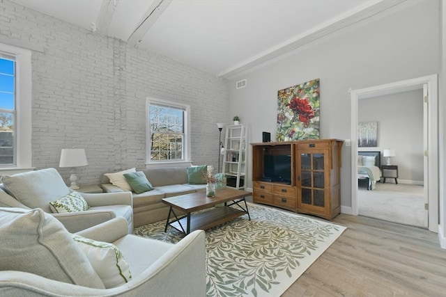 living room with brick wall, light wood-type flooring, visible vents, and baseboards