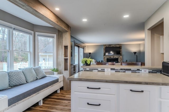 kitchen with open floor plan, white cabinets, dark wood-style flooring, a peninsula, and a stone fireplace