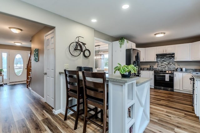 kitchen with electric stove, refrigerator with ice dispenser, range hood, white cabinets, and healthy amount of natural light