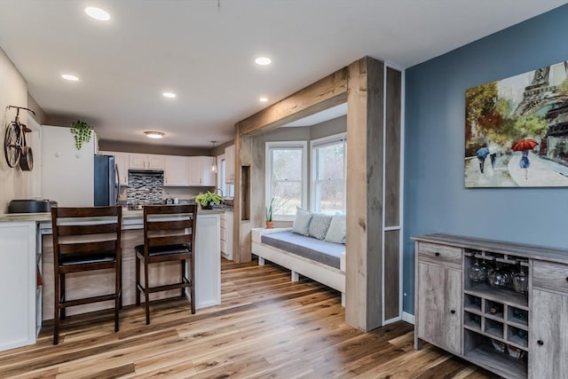 kitchen with white cabinets, light wood-style floors, fridge, recessed lighting, and a breakfast bar