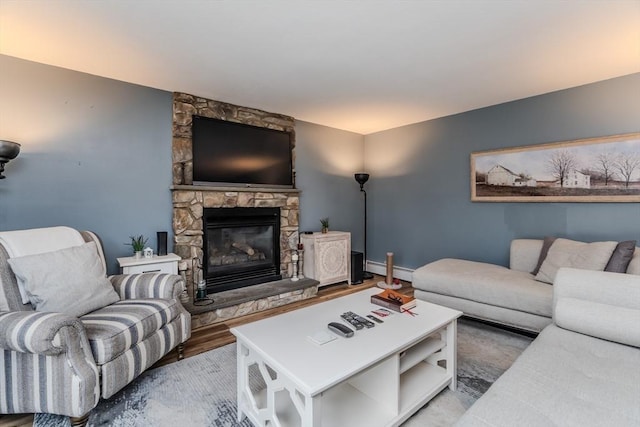 living room featuring a baseboard heating unit, a stone fireplace, and wood finished floors