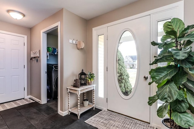 foyer entrance featuring baseboards, dark tile patterned floors, and washer / dryer