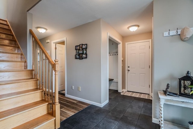 foyer entrance with stairway, baseboards, and dark tile patterned flooring