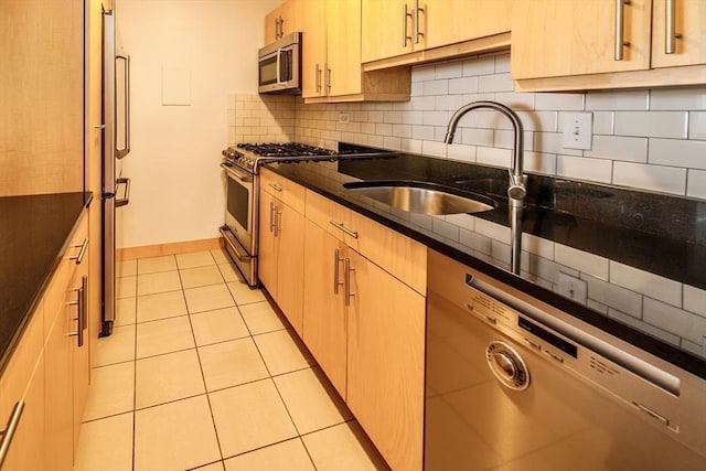 kitchen with dark stone countertops, light tile patterned floors, a sink, decorative backsplash, and appliances with stainless steel finishes