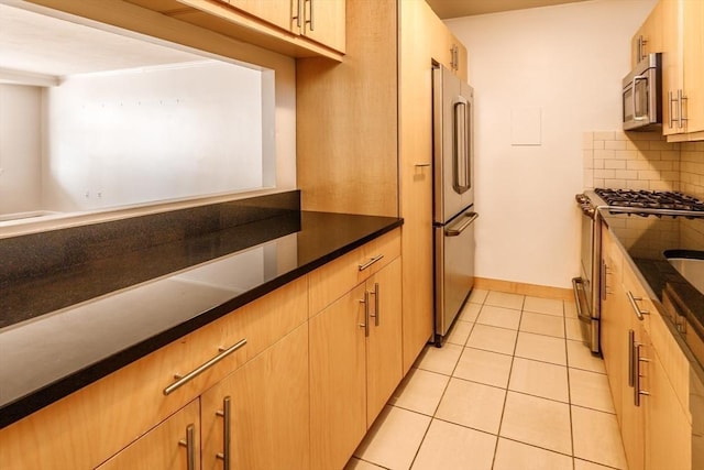 kitchen featuring light tile patterned flooring, decorative backsplash, appliances with stainless steel finishes, and baseboards