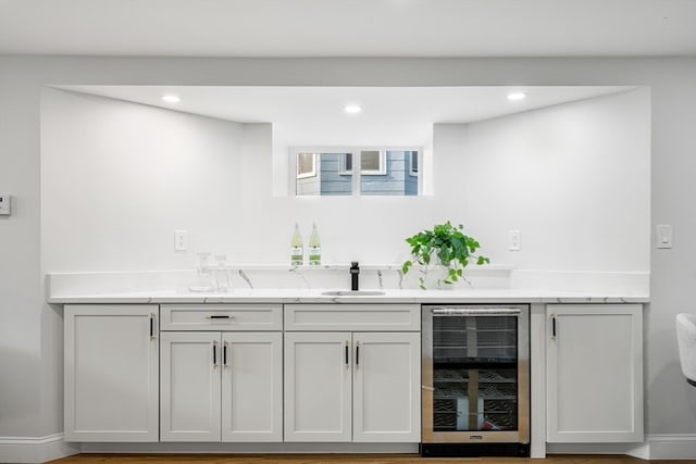 bar featuring white cabinets, wine cooler, sink, light stone countertops, and hardwood / wood-style floors