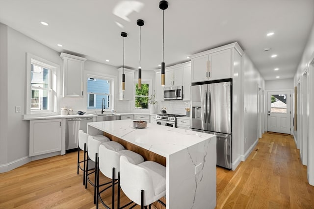 kitchen with stainless steel appliances, white cabinets, a kitchen island, and light wood-type flooring