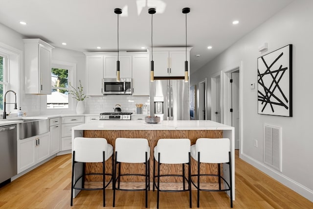 kitchen with a kitchen island, light wood-type flooring, stainless steel appliances, pendant lighting, and white cabinetry