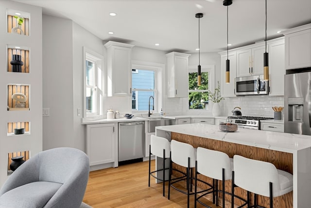 kitchen featuring light hardwood / wood-style floors, a kitchen island, stainless steel appliances, hanging light fixtures, and white cabinets