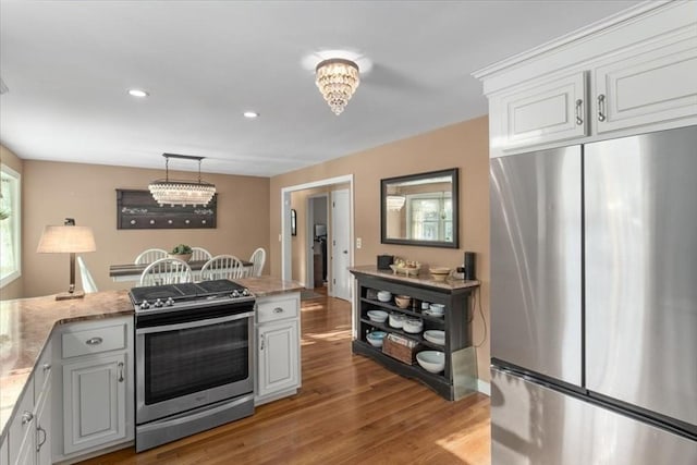 kitchen featuring hanging light fixtures, light stone countertops, appliances with stainless steel finishes, and white cabinets