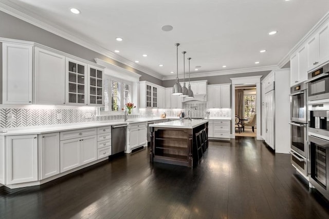 kitchen featuring white cabinetry, appliances with stainless steel finishes, hanging light fixtures, and a center island with sink