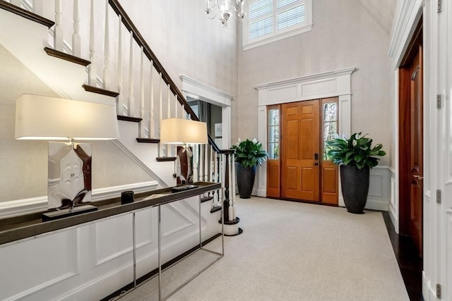 entryway with a notable chandelier, light colored carpet, and a high ceiling