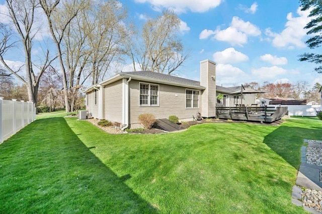 back of house with fence, a deck, cooling unit, a chimney, and a lawn