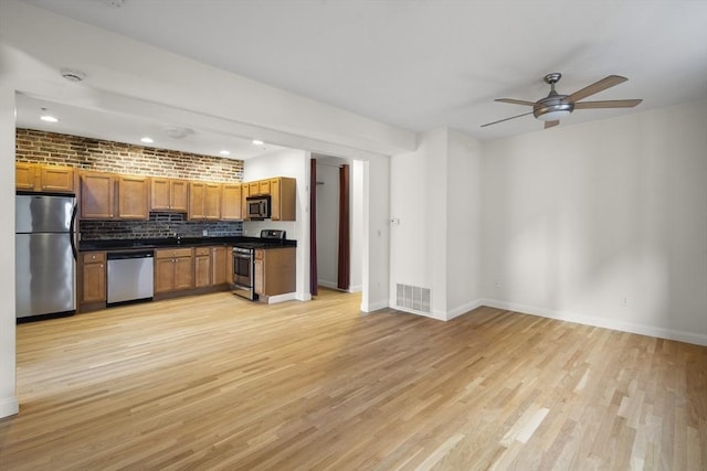 kitchen featuring ceiling fan, light wood-style floors, dark countertops, stainless steel appliances, and tasteful backsplash