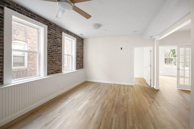 spare room with light wood finished floors, baseboards, ceiling fan, and brick wall