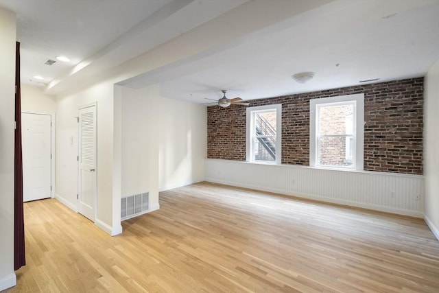 unfurnished room with a ceiling fan, light wood-style flooring, baseboards, brick wall, and visible vents