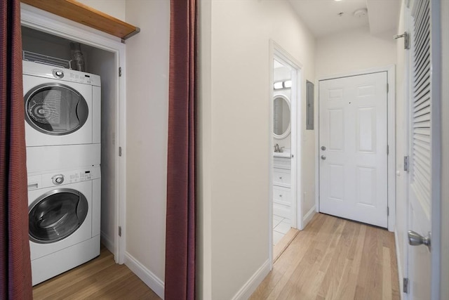 clothes washing area with baseboards, stacked washer and dryer, laundry area, and light wood-style floors