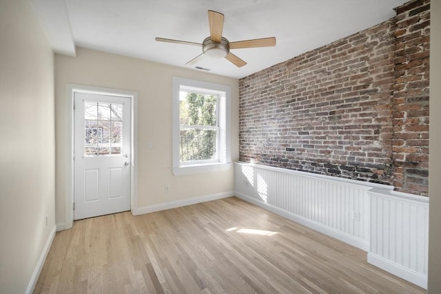 interior space with a ceiling fan, brick wall, visible vents, baseboards, and light wood-style floors