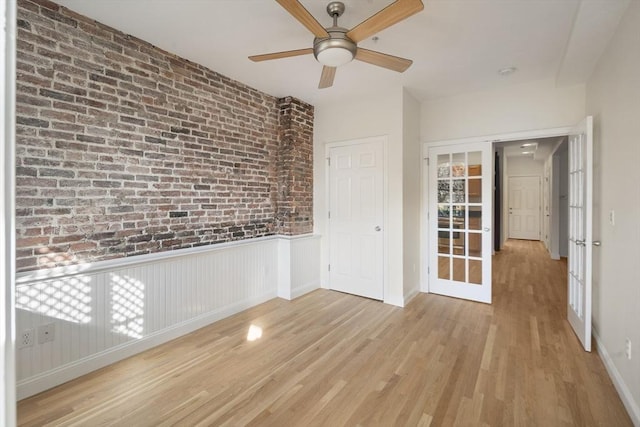 unfurnished room with wood finished floors, baseboards, ceiling fan, and brick wall