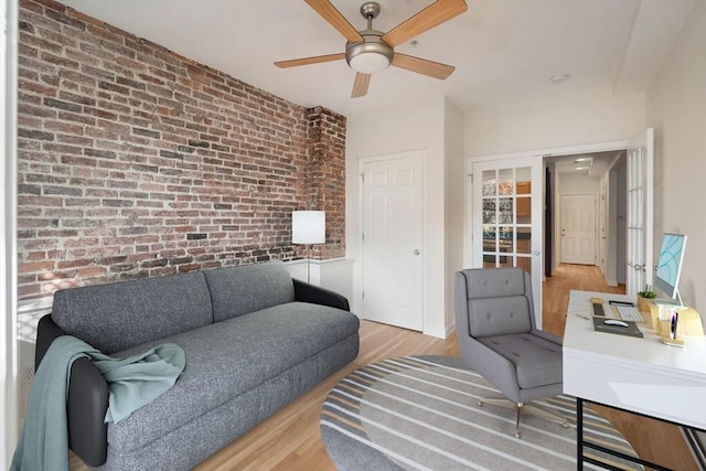 living area featuring brick wall, light wood-type flooring, and a ceiling fan