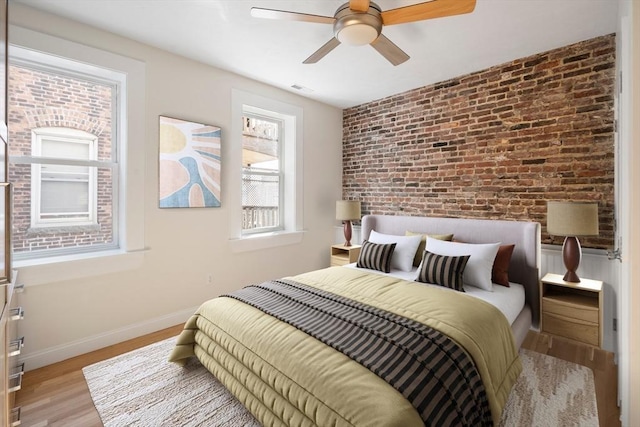 bedroom featuring wood finished floors, a ceiling fan, brick wall, visible vents, and baseboards
