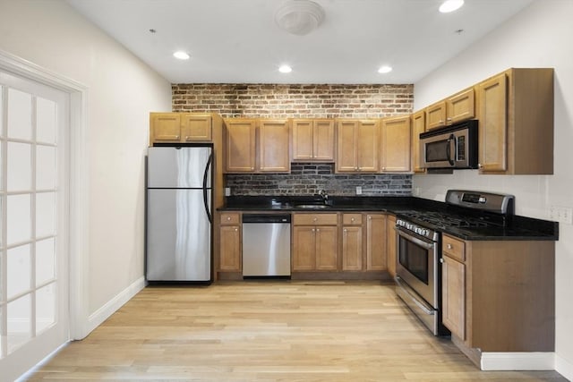 kitchen featuring baseboards, a wealth of natural light, a sink, stainless steel appliances, and light wood-type flooring