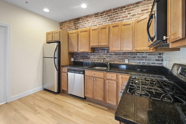 kitchen featuring a sink, stainless steel appliances, dark stone counters, decorative backsplash, and baseboards