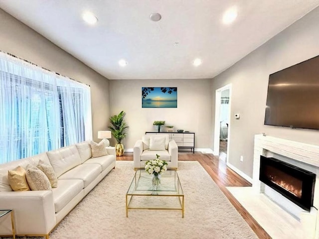 living room featuring a fireplace with flush hearth, wood finished floors, baseboards, and recessed lighting
