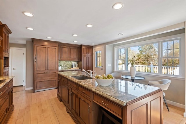 kitchen with light wood-style floors, tasteful backsplash, light stone counters, and a sink