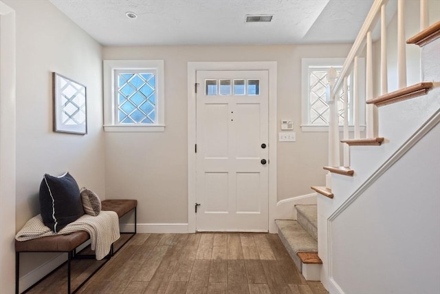 foyer featuring baseboards, visible vents, wood finished floors, stairs, and a textured ceiling