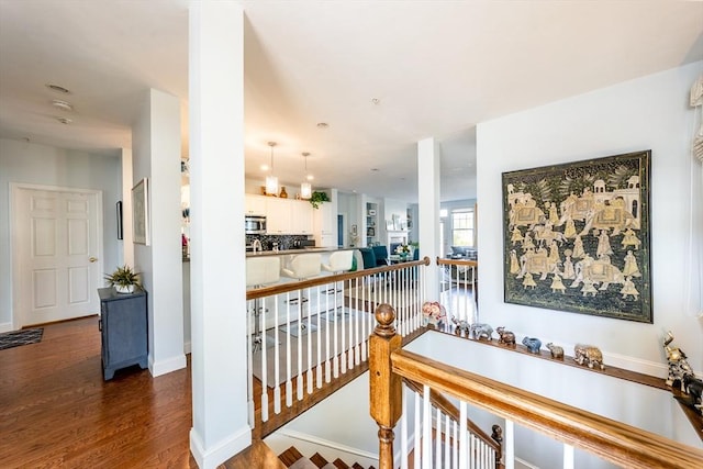 corridor featuring baseboards, wood finished floors, and an upstairs landing