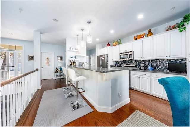 kitchen with tasteful backsplash, appliances with stainless steel finishes, a breakfast bar area, dark wood-type flooring, and white cabinetry