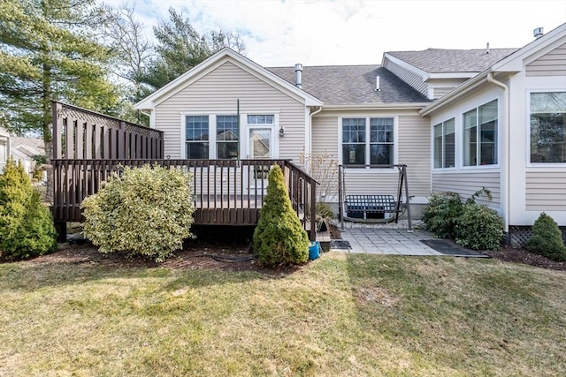 back of property with a deck, a yard, a shingled roof, and a patio